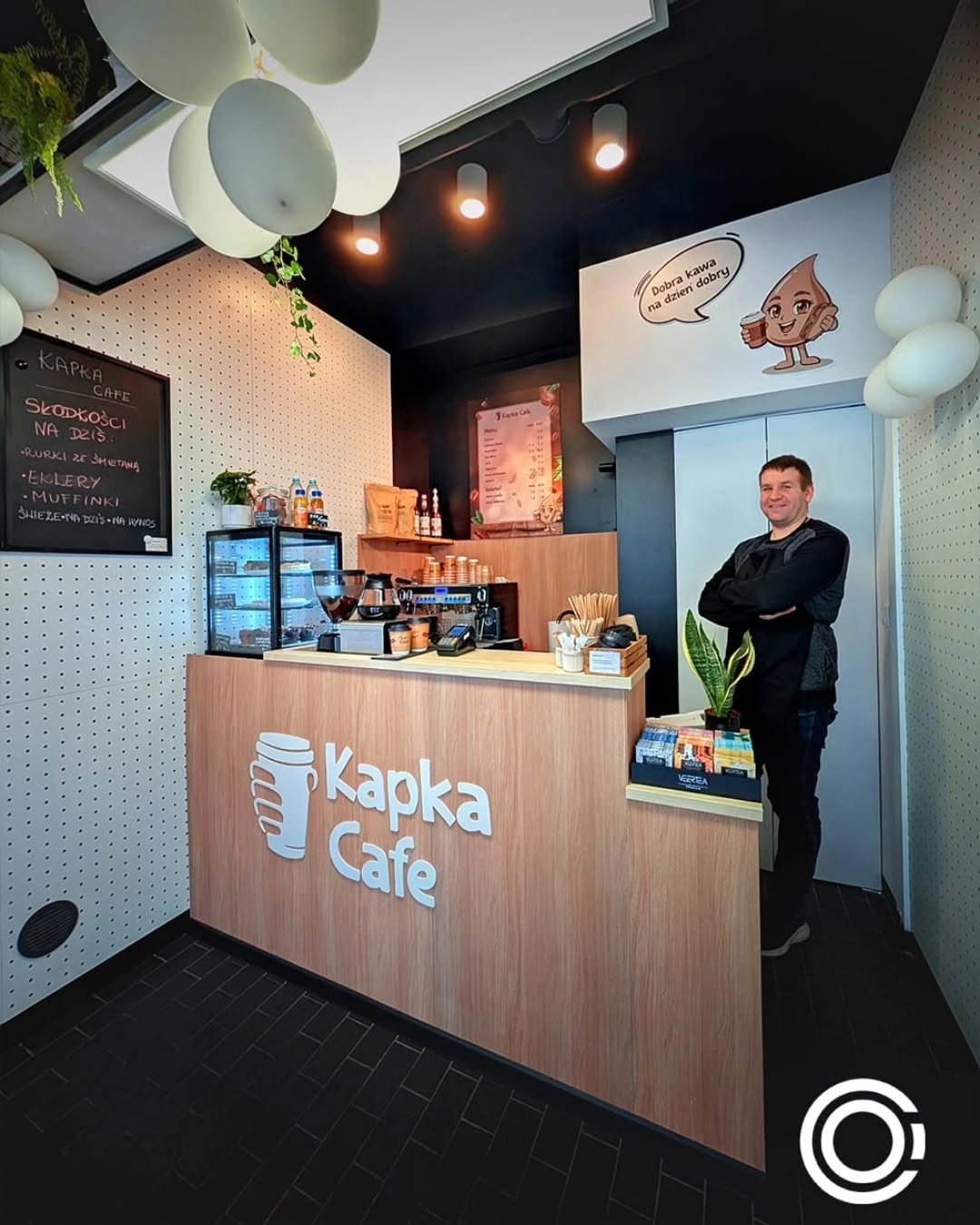 Wnętrze Kapka Cafe: lada z przestrzennym logo i naklejka z maskotką na ścianie